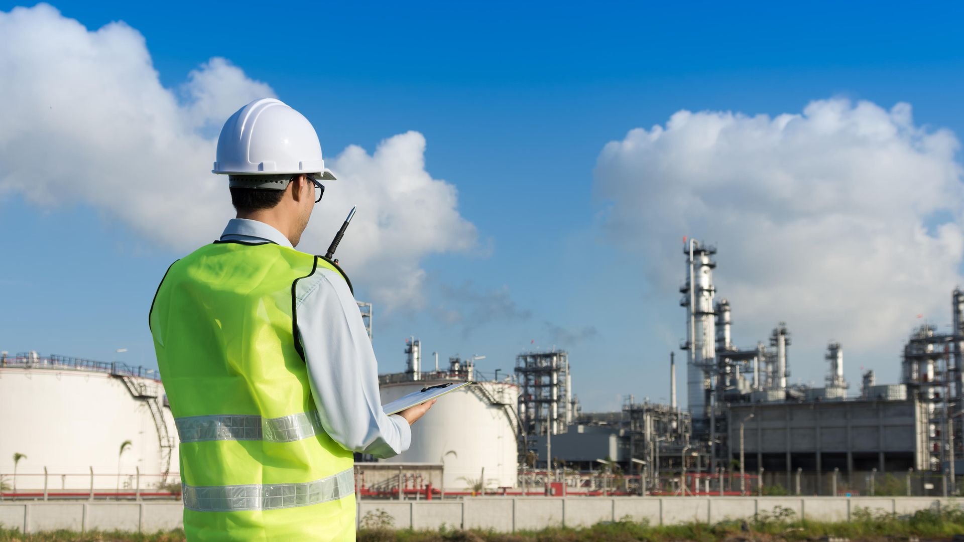 Trabajador de refinería gestionando y administrando recursos chaleco casco portapapeles planta walkie talkie